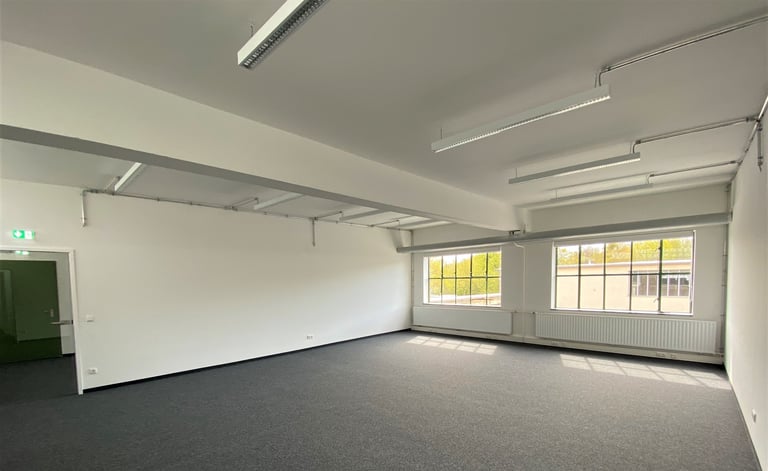 Leere Büro- oder Gewerbefläche mit weißen Wänden, grauem Boden, Deckenleuchten und großen Fenstern
