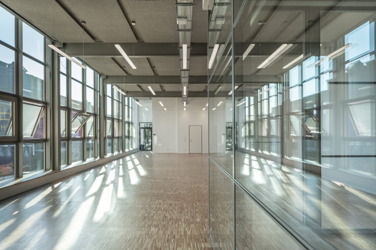 Moderner leerer Büroflur mit bodentiefen Fenstern, weißen Deckenpaneelen und natürlichem Lichteinfall auf Holzboden