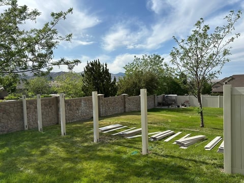 Residential construction site with concrete foundation posts and white pillars on grassy lawn surrounded by stone wall and trees