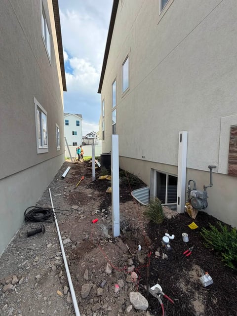 Construction site between two beige residential buildings with utility lines and equipment scattered on the ground