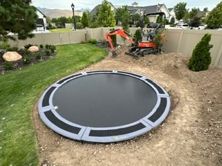 In-ground trampoline installation in backyard with construction equipment and landscaping visible.