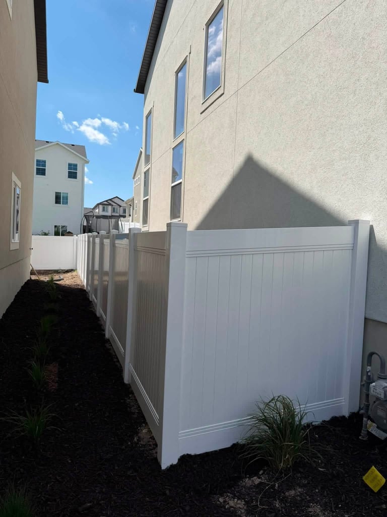 White vinyl privacy fence panels between residential buildings with landscaping and blue sky