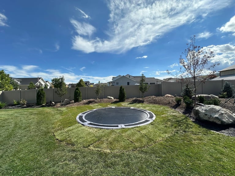 Backyard trampoline on green lawn with mountains and blue sky in background