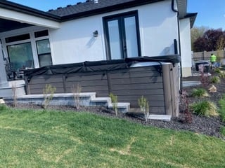 Modern white house with dark gray pergola over patio area, landscaped garden beds with plants, and manicured lawn
