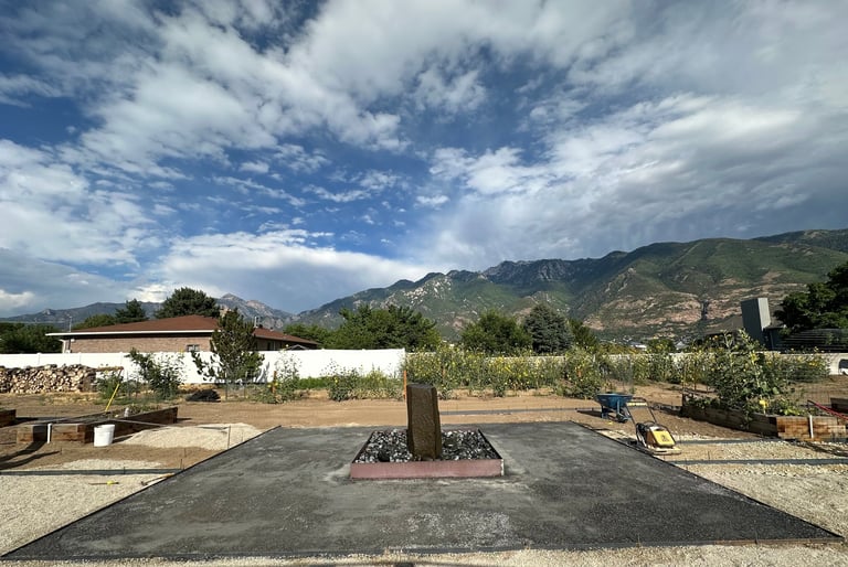 Courtyard with paved ground, central tree, white building, and mountain range under blue sky with clouds