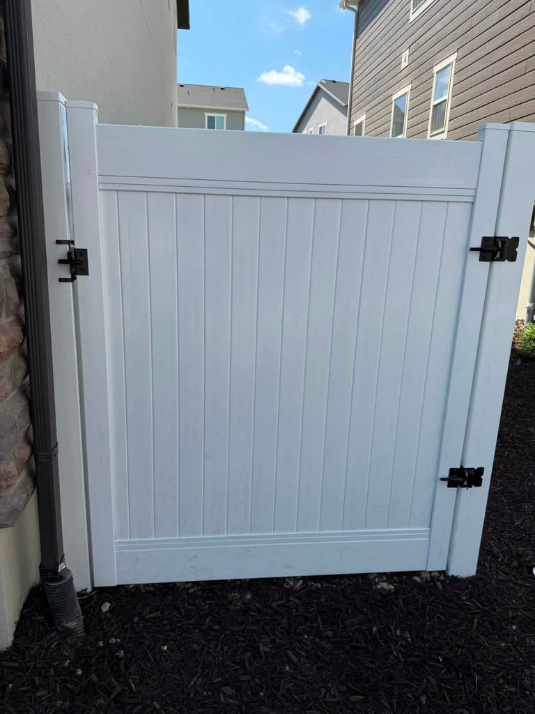 White vinyl gate with vertical panels and black hinges installed between residential buildings