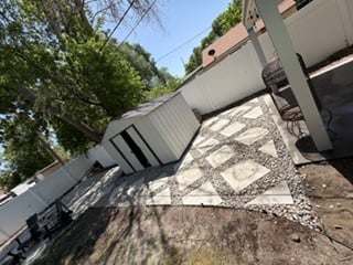 Paver patio in progress with concrete pavers being laid in a pattern with gravel base and patio chairs nearby
