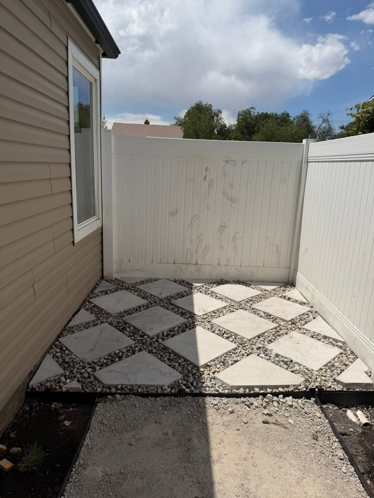 Backyard patio with white vinyl fence and decorative concrete pavers in a diamond pattern with gravel accents