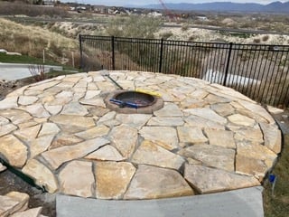 Stone fire pit on a circular patio with metal railing overlooking hills and mountains