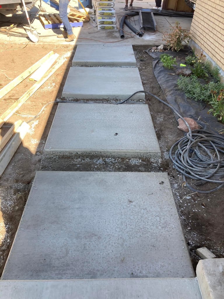 Concrete stepping stones laid out in a construction area with tools, equipment, and a coiled garden hose visible nearby