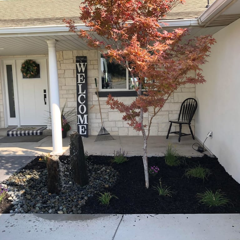 Home entrance with red maple tree, welcome sign, black gravel landscaping, and porch seating area