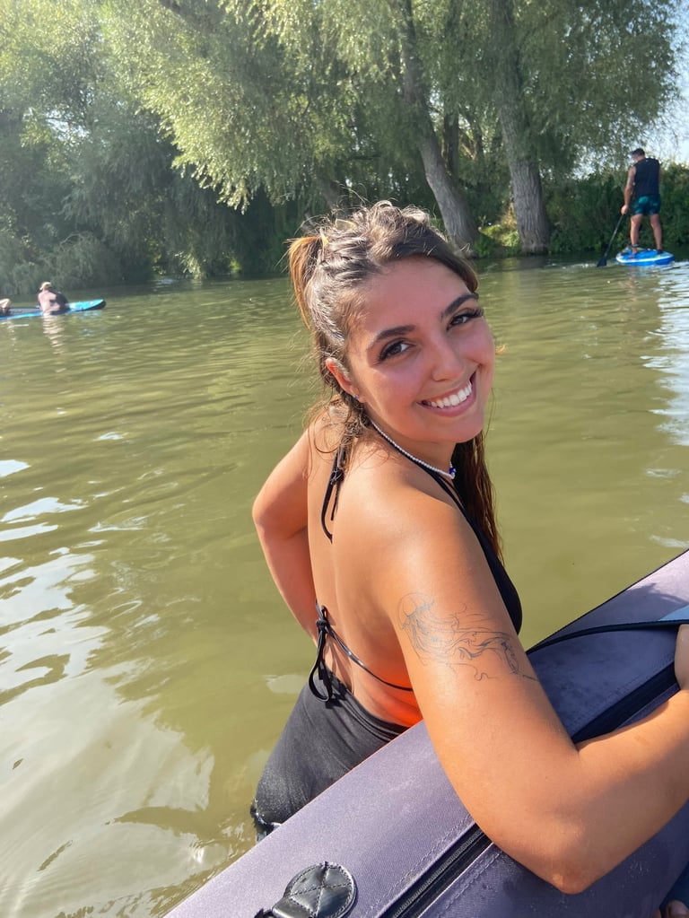 Ines smiling on a paddleboard in a calm river surrounded by trees
