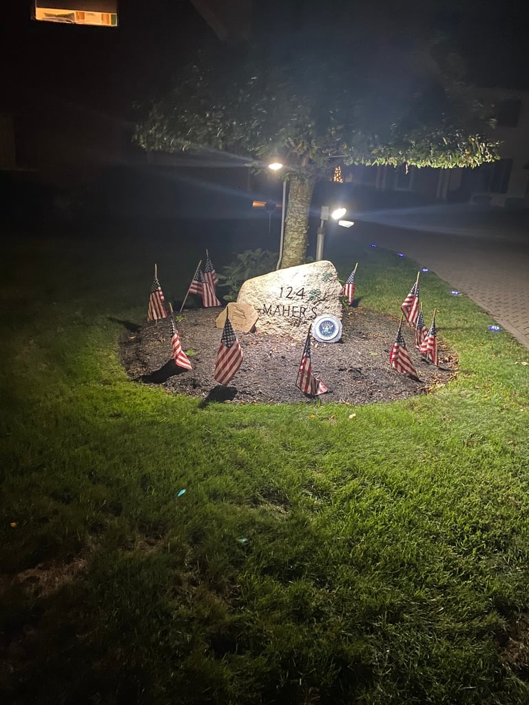 Memorial marker surrounded by American flags illuminated at night on a grassy lawn
