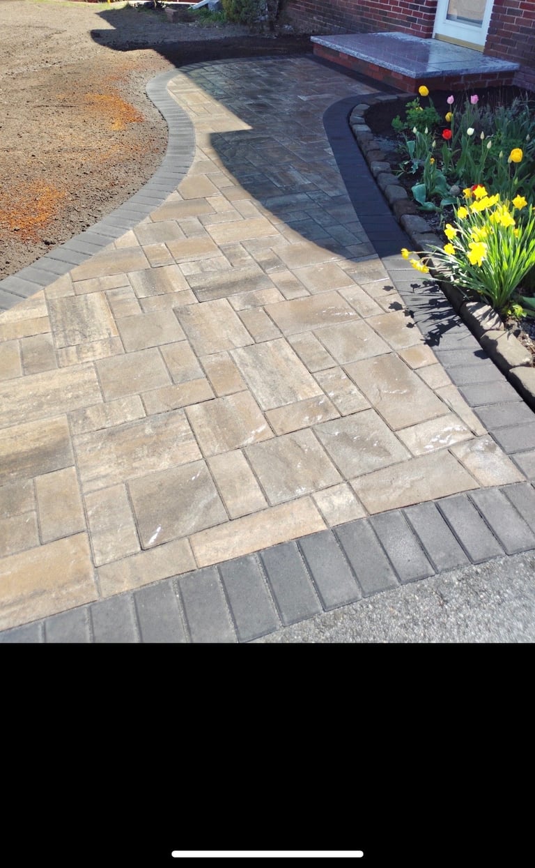 Residential patio with herringbone paver pattern, colored flower beds with red and yellow tulips, and curved landscaping edging