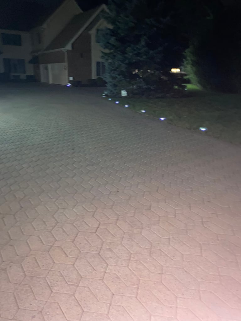 Nighttime driveway with stone paving lit by small ground lights leading to a residential house with garage