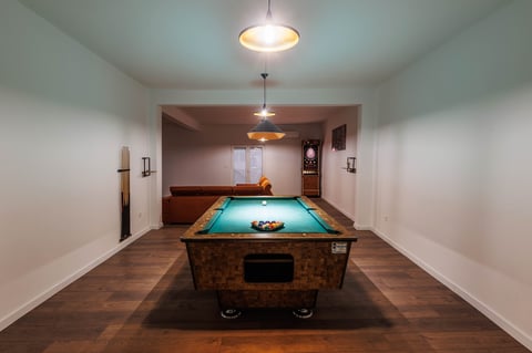 Pool table with turquoise felt in a finished basement recreation room with wooden floors and pendant lighting