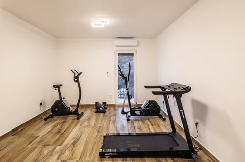 Home gym with treadmill in foreground, stationary bike on left, and elliptical machine on right, all on wooden floor in bright room
