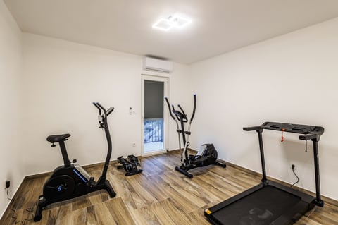 Modern home gym with exercise bikes, elliptical machine, treadmill, and wooden flooring in a bright, minimalist room