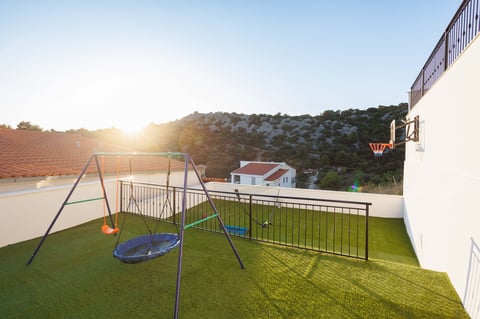 Sunny rooftop garden with blue swing and basketball hoop on artificial lawn