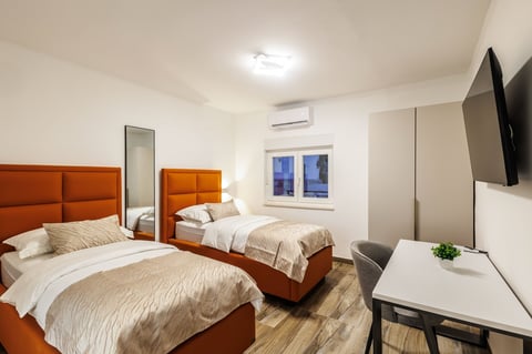 Twin bedroom with orange beds, wall-mounted TV, and large windows