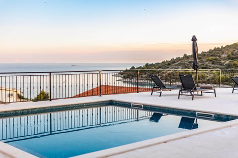 A modern swimming pool with lounge chairs overlooking a coastal landscape at sunset