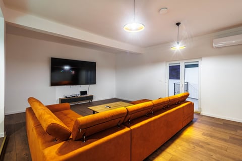 Modern living room with a large orange sectional sofa facing a wall-mounted TV and wooden flooring