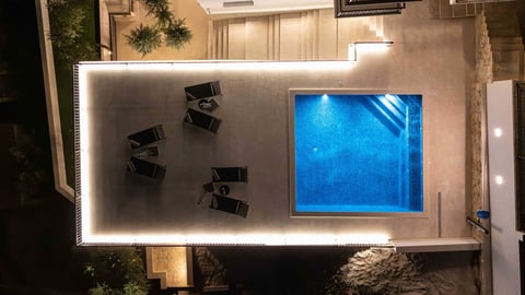 Overhead view of a modern pool with illuminated deck, lounge chairs, and blue water at night