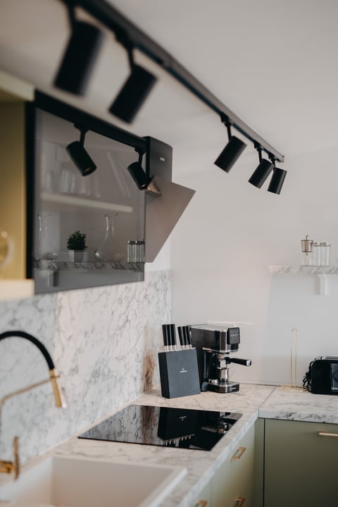 Modern minimalist kitchen with marble backsplash, black track lighting, espresso machine, and sage green cabinetry