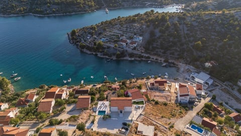Aerial view of a coastal village with terracotta-roofed houses on a hillside overlooking turquoise waters with boats