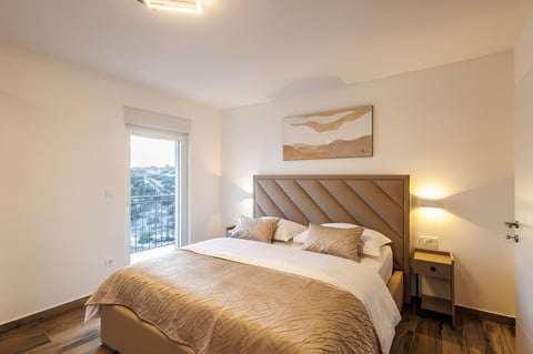 Modern bedroom with beige decor, wooden headboard, and balcony view
