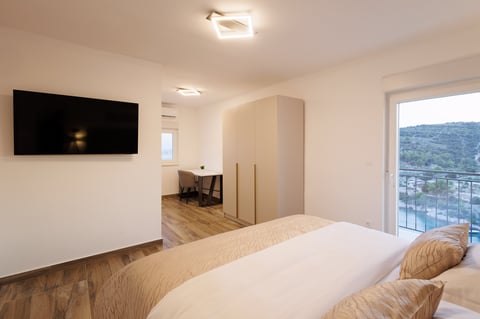 Modern bedroom with bed, wall-mounted TV, work desk, sliding glass door overlooking mountain view, and wood flooring
