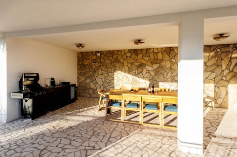 Modern residential interior with stone accent wall, wooden dining table, black kitchen area, and geometric patterned flooring