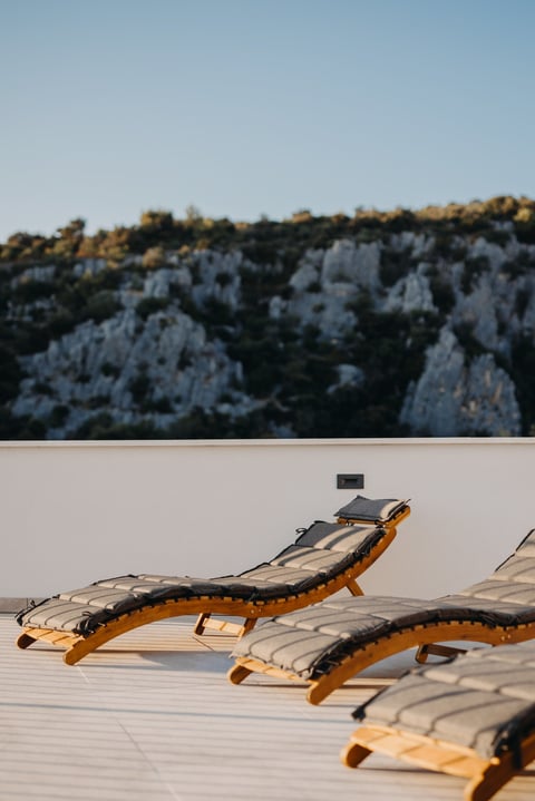 Wooden lounge chairs with gray cushions arranged on a white deck overlooking rocky cliffs and forest