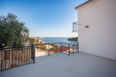 Empty modern terrace with metal railing overlooking a blue sea and coastal landscape under clear sky