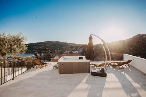 Rooftop terrace overlooking hills with modern furniture, hot tub, and lounge chairs during sunset