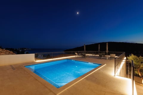 Illuminated swimming pool at night with mountain backdrop and starry sky