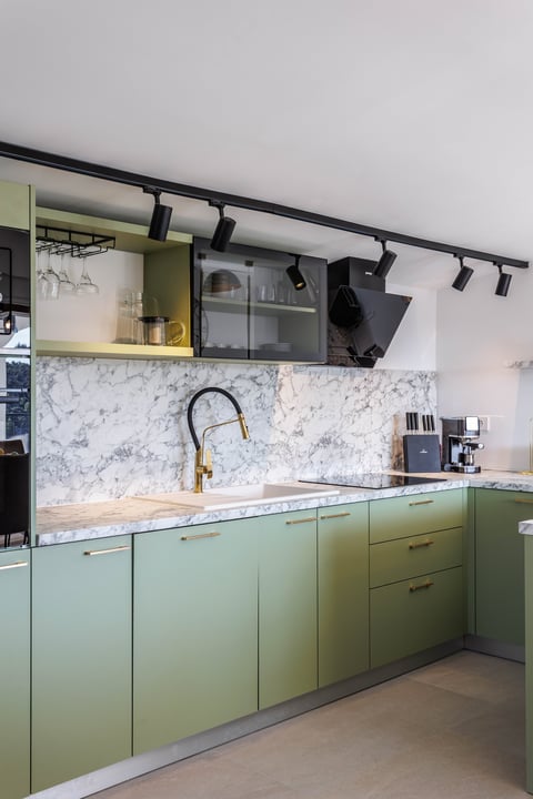 Modern kitchen with sage green cabinets, marble backsplash, black track lighting, and minimalist design
