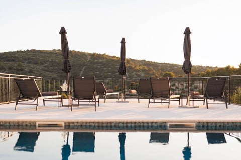 Swimming pool with lounge chairs and black umbrellas on a sunny deck overlooking green hills