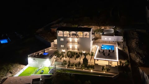 Aerial nighttime view of an illuminated modern residential complex with manicured landscaping and outdoor amenities