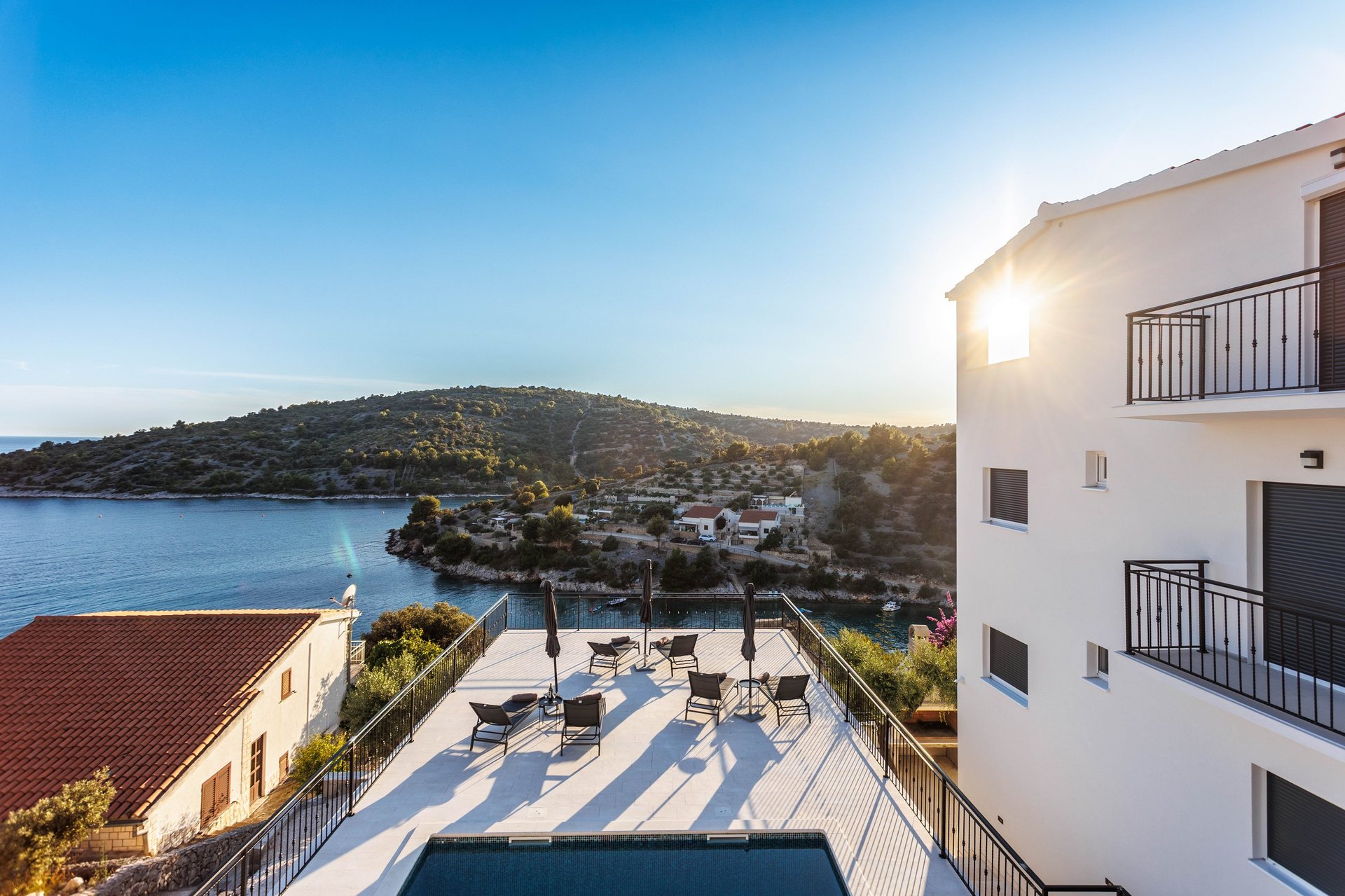 Modern white Villa Forte with pool deck overlooking a coastal bay surrounded by hills at sunset