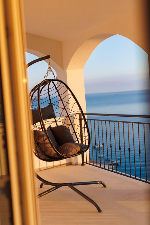Hanging egg chair on a beachfront balcony with ocean view through arched white doorway