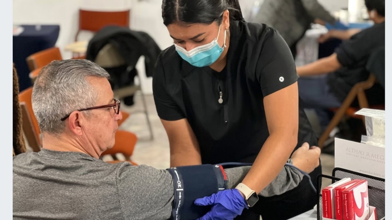 Healthcare worker in mask and gloves administering vaccine to seated elderly man wearing glasses