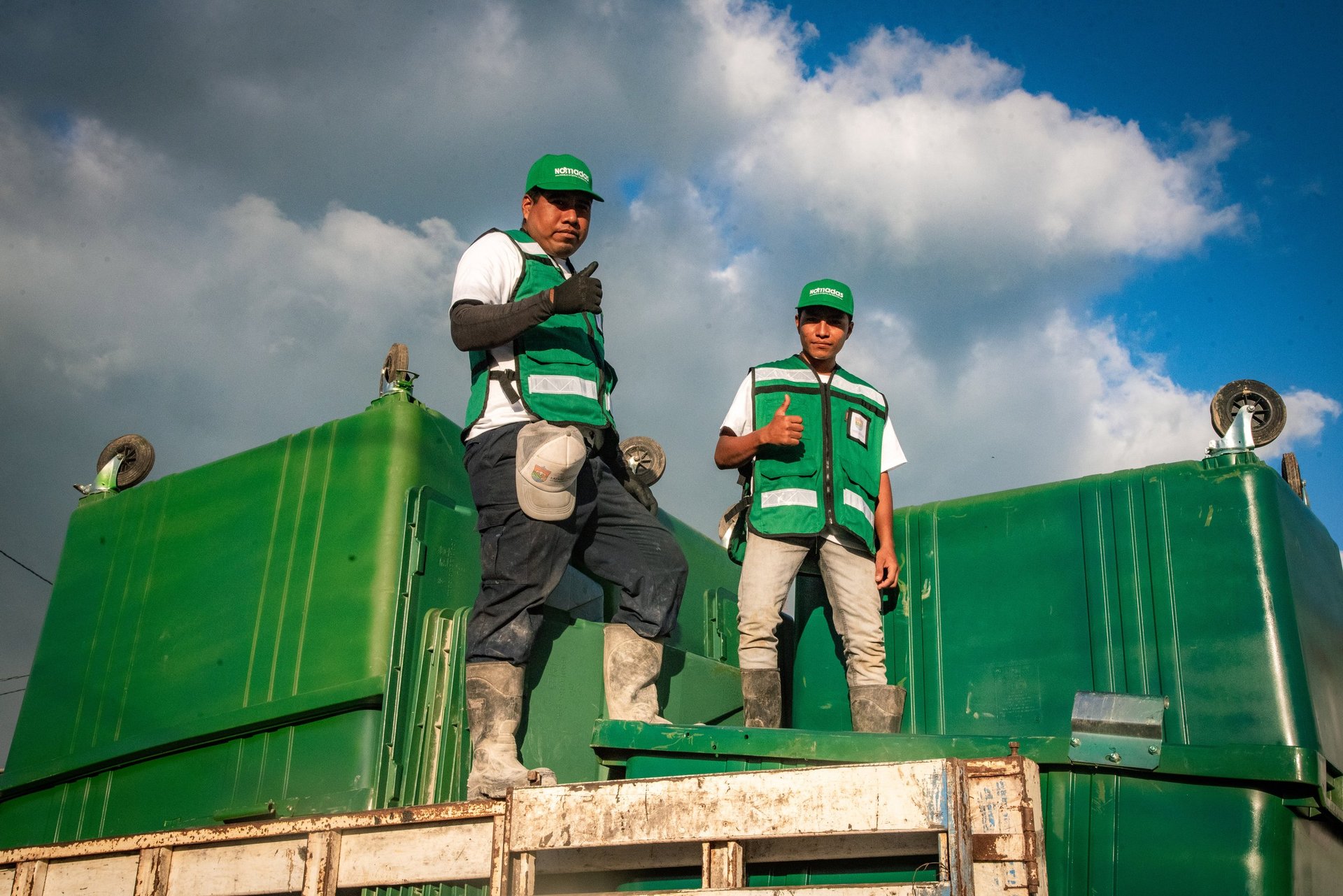 Tres trabajadores con chalecos verdes NÓMADAS parados sobre un contenedor verde de carga