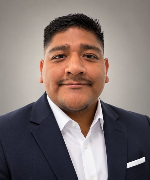 Professional headshot of a man with dark hair and mustache wearing a navy blazer and white dress shirt against a gray background
