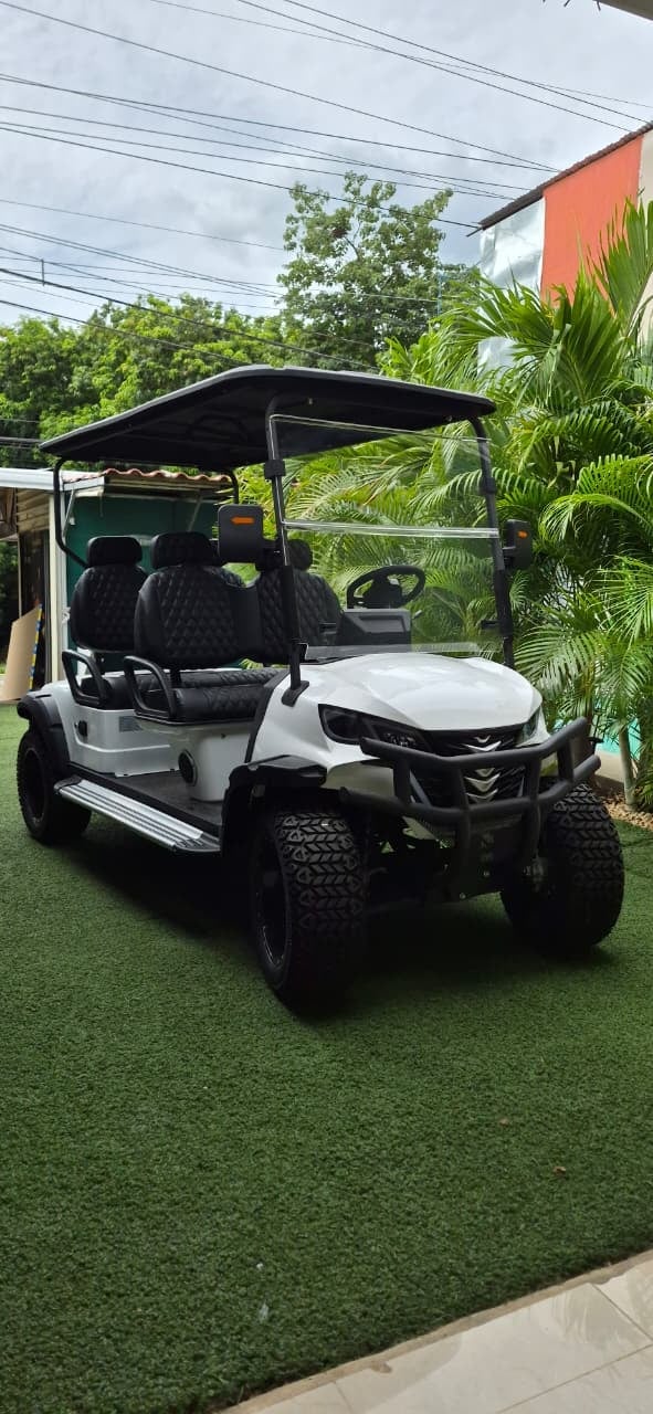 White and black golf cart with black canopy parked on artificial green turf in a tropical residential setting