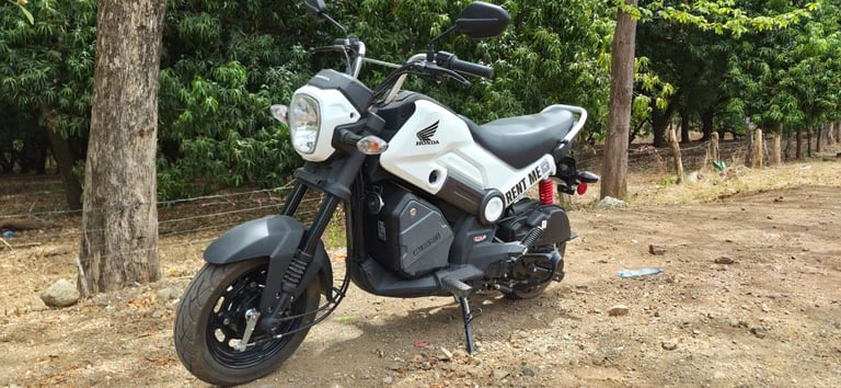 White and black Honda Navi scooter parked on dirt ground with trees in the background