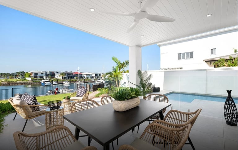 Modern covered patio with dining table, woven chairs, and pool overlooking waterfront neighborhood