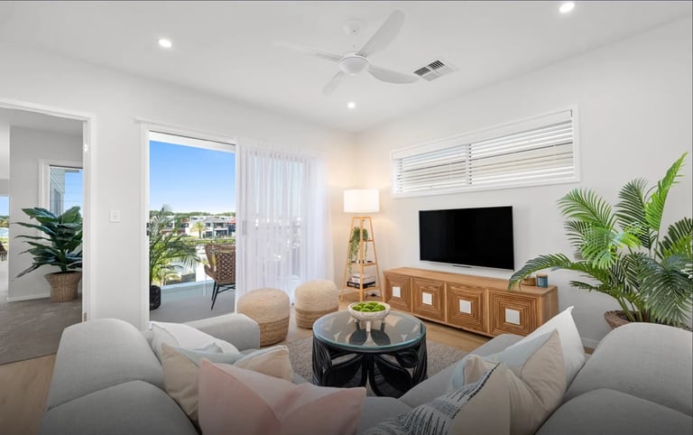 Modern living room with gray seating, TV console, potted plants, and sliding glass doors overlooking a balcony