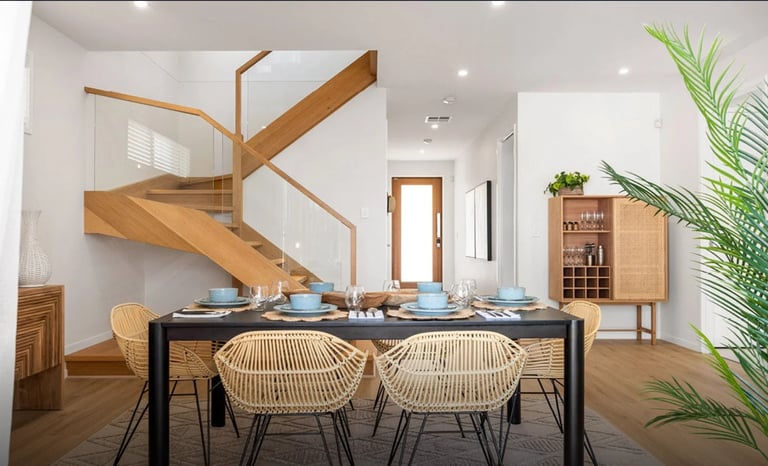 Modern dining room with wooden staircase, black dining table, woven chairs, and potted plants
