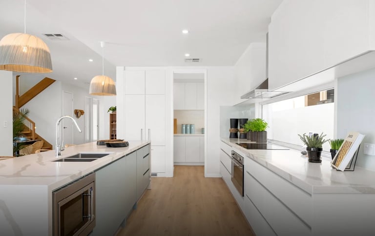 Modern white kitchen with island, pendant lights, stainless steel appliances, and potted plants
